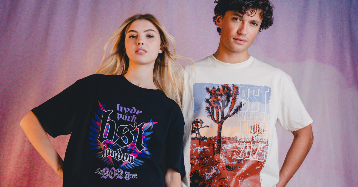 A woman wearing a black graphic tee and a man in a white graphic tee stand side by side, looking at the camera, with a pastel-colored background behind them.